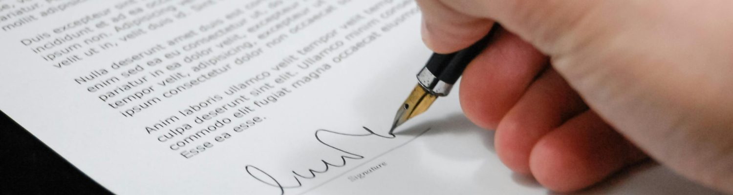 Close-up of a hand signing a legal document with a fountain pen, symbolizing signature and agreement.